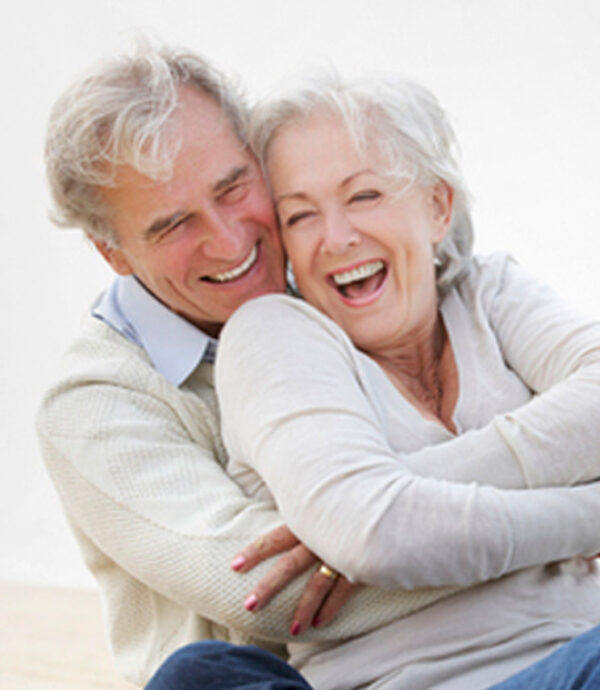 Um casal de idade avançada se abraçando e sorrindo.