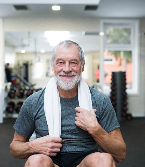 Senhor de idade com toalha branca no pescoço sorrindo em uma academia.